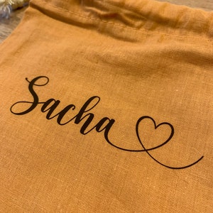 Peut inclure: Un sac en tissu marron à cordon avec le nom "Sacha" et un cœur brodé.