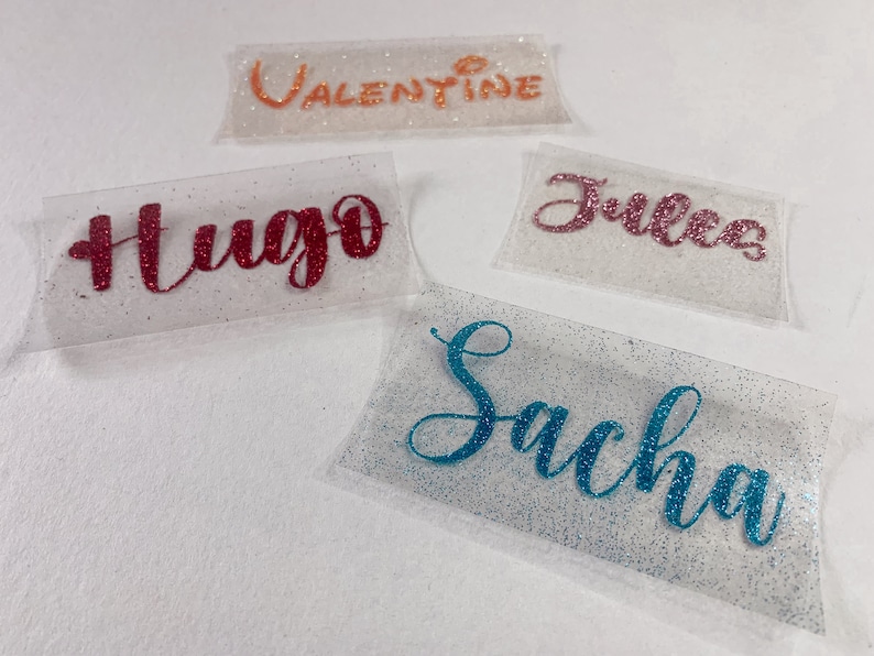 May include: Four clear plastic gift bags with glitter accents. The bags are decorated with the names "Valentine", "Hugo", "Jules", and "Sacha" in different coloured glitter.