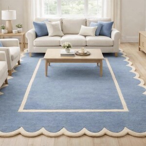 May include: A light blue rug with a scalloped edge and a cream-colored border. The rug is in a living room setting with a sofa, chairs, and a coffee table. The rug's dimensions are approximately 8 x 10 feet.