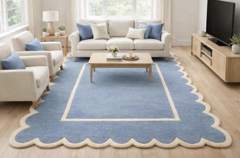May include: A light blue rug with a scalloped edge and a cream-colored border. The rug is in a living room setting with a sofa, chairs, and a coffee table. The rug's dimensions are approximately 8 x 10 feet.