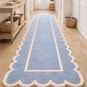 May include: A light blue runner rug with a scalloped edge and a cream-colored border. The rug is rectangular and placed on a hardwood floor. The rug's design adds a touch of elegance to the hallway.