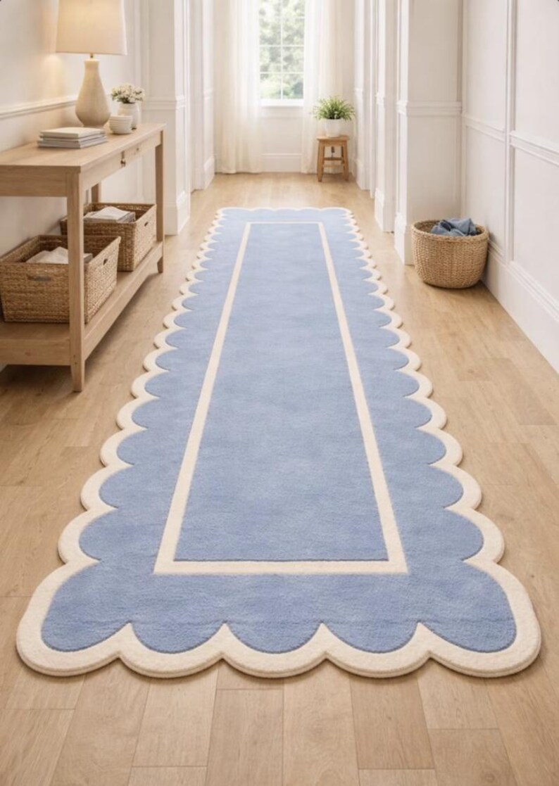May include: A light blue runner rug with a scalloped edge and a cream-colored border. The rug is rectangular and placed on a hardwood floor. The rug's design adds a touch of elegance to the hallway.