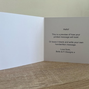 May include: An open, white greeting card with text that reads "Hello! This is a preview of how your printed message will look!" and "Love from, Belle & Fi Designs x."