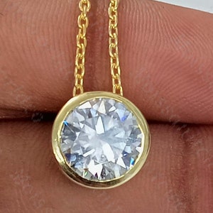 Op de afbeelding: Een gouden ketting met een ronde, bezel-gezet, heldere edelsteen hanger.