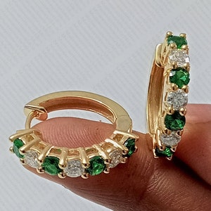 May include: A pair of gold hoop earrings with alternating green and white round stones.