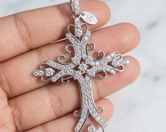 May include: A silver-toned cross pendant featuring intricate filigree scrollwork and pavé-set clear stones throughout the design. The pendant includes a small oval tag engraved with the letter E attached to the top bail, creating a detailed piece.