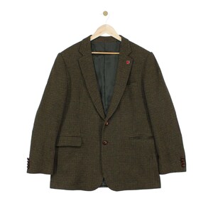 May include: A dark olive green and black houndstooth blazer featuring a notched lapel, two front buttons, two flap pockets, and four buttons on each sleeve cuff. The interior is lined with a dark green fabric and includes a small red lapel pin.
