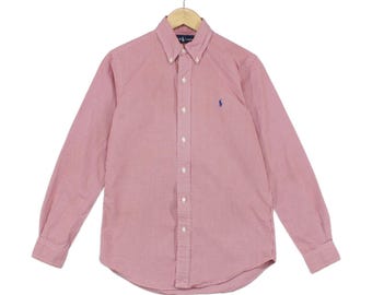 May include: A long-sleeve button-down shirt in a red and white micro-check pattern. The shirt features a button-down collar, a front button placket, and a small blue embroidered logo on the left chest. It is displayed on a wooden hanger.