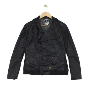 May include: A black G-Star Raw jacket featuring a button-up front closure, a high collar, and long sleeves. The garment includes a ribbed hem, shoulder epaulets, and a small yellow brand label on the lower front panel, all displayed on a hanger.
