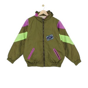 Peut inclure: Une veste zippée vert olive avec une capuche, des manches longues à rayures color-block violettes et jaune fluo, et deux poches avant à bordure violette. Un écusson rectangulaire avec du texte bleu et blanc est centré sur la poitrine.
