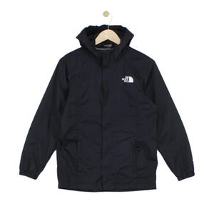Op de afbeelding: Een zwarte jas met capuchon, voorzien van een ritssluiting aan de voorzijde, lange mouwen met elastische boorden en twee zijzakken. Het witte logo van The North Face staat op de linkerborst. De jas hangt aan een houten kledinghanger.