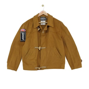 May include: A tan wool-blend duffle jacket featuring a classic collar, long sleeves, and two wooden toggle closures with rope loops. The jacket includes a Gloverall brand tag with a Union Jack flag graphic and a label reading Made in England.