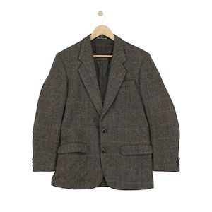 May include: A brown and olive green tweed blazer featuring a subtle plaid pattern, notched lapels, two front buttons, two flap pockets, and a chest pocket. The jacket is lined in dark brown fabric and includes a label stating Made in England.