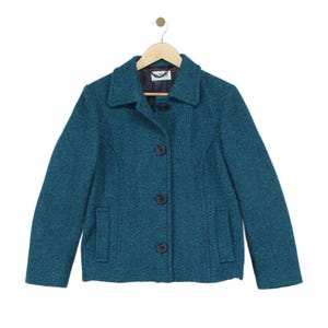 May include: A teal textured jacket featuring a classic collar, long sleeves, and a front button closure with four dark buttons. The jacket includes two front pockets and a dark interior lining with a visible label reading JAMES at the neckline.