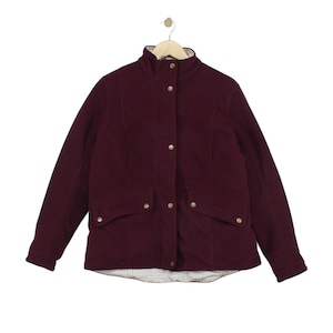 May include: A deep burgundy jacket featuring a high collar, long sleeves, and a front placket with metallic snap buttons. The jacket includes two front flap pockets with snap closures and a visible white and black grid-patterned interior lining.