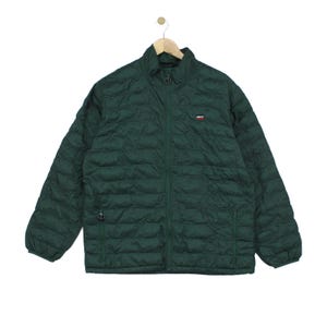 Può includere: Una giacca imbottita trapuntata verde scuro con collo alto e chiusura frontale con zip. La giacca presenta maniche lunghe con polsini elastici, due tasche laterali con zip e un piccolo logo del marchio Levi's sulla parte sinistra del petto.