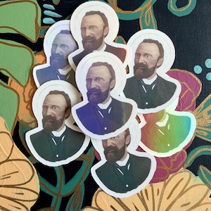 以下が含まれることがあります： ひげと光輪のある男性の肖像画が描かれたステッカーのコレクション。ステッカーは、オレンジ、緑、ピンクの色合いのフローラルデザインの背景に配置されています。男性はダークスーツを着ています。