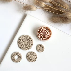 Może przedstawiać: Zestaw czterech beżowych glinianych kół o skomplikowanych geometrycznych wzorach. Największe koło ma wypukły wzór i jest jasnoróżowe.