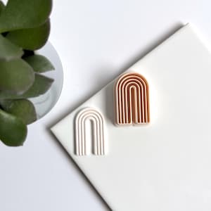Op de afbeelding: Twee roze en witte plastic regenboog boog koekjesuitstekers. De grotere uitsteker is donkerroze en de kleinere is lichtroze.