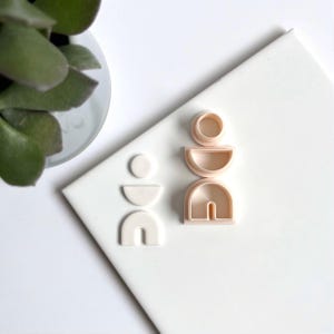 Op de afbeelding: Een set van vijf witte en roze plastic koekjesvormen in de vorm van geometrische figuren. De vormen zijn gerangschikt op een wit oppervlak.