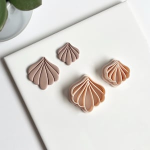 Può includere: Quattro taglierini in argilla polimerica a forma di conchiglia di varie dimensioni, esposti su una superficie bianca. I taglierini sono in tonalità beige e marrone, con dettagliate creste a forma di ventaglio. Ideali per l'artigianato.