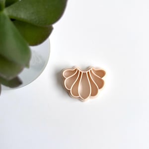 Op de afbeelding: Een lichtroze plastic koekjesvormpje in de vorm van een schelp met een decoratief ontwerp.