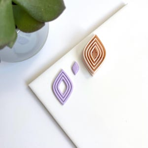 Op de afbeelding: Twee sets van gelaagde diamantvormen gemaakt van polymer clay. De ene set is in tinten perzik en de andere is in tinten lavendel.