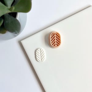 Peut inclure: Deux petites décorations en céramique en forme de feuille. L'une est blanche avec un motif de feuille en relief et l'autre est pêche avec un motif de feuille découpé.