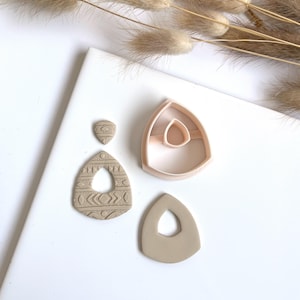 Op de afbeelding: Een set van drie polymer clay oorsteker uitstekers. De uitstekers zijn in de vorm van een traan met een kleinere traan uitgesneden in het midden. De uitstekers zijn beige van kleur.