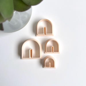 Peut inclure: Ensemble de quatre emporte-pièces en plastique en forme d'arches avec une découpe au centre. Les emporte-pièces sont de tailles différentes et sont de couleur pêche clair.