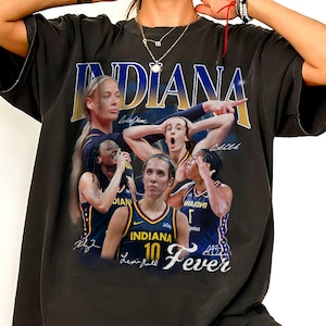 Op de afbeelding: Een zwart t-shirt met korte mouwen en een grafische print van Indiana Fever basketbalspeelsters in marineblauwe en gele uniformen. Het ontwerp bevat de tekst INDIANA en Fever, samen met meerdere afbeeldingen van speelsters en gestileerde handtekeningen.