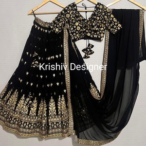 Op de afbeelding: Zwarte geborduurde rok en bijpassend top met gouden draad, en een zwarte, doorschijnende dupatta met gouden bies. De outfit wordt getoond op een hanger. De tekst "Krishiv Designer" is zichtbaar op de rok.