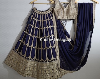 Può includere: Un abito da sposa indiano blu navy e oro con gonna, blusa e dupatta. La gonna ha un design ricamato in oro e la blusa ha una scollatura a V. Il dupatta è un tessuto trasparente con un bordo dorato.