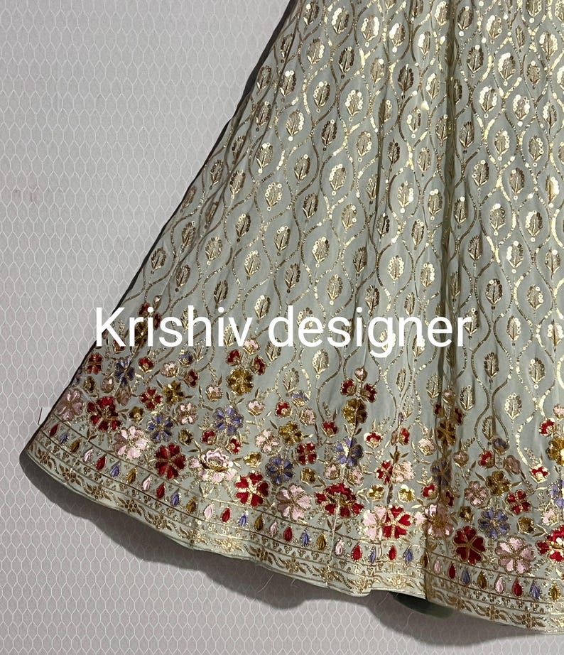May include: A light green skirt with a floral pattern and gold sequins. The skirt has a scalloped hemline and is decorated with colourful embroidery.