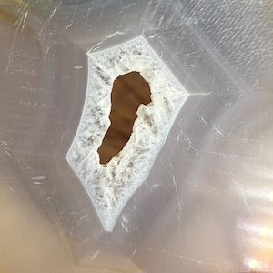 May include: Close-up of a white agate slice with a large, irregular hole in the centre. The hole is surrounded by a white, crystalline edge.