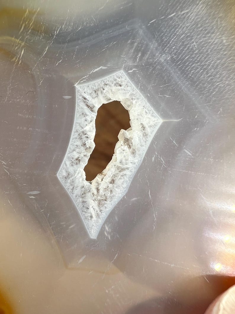 May include: Close-up of a white agate slice with a large, irregular hole in the centre. The hole is surrounded by a white, crystalline edge.