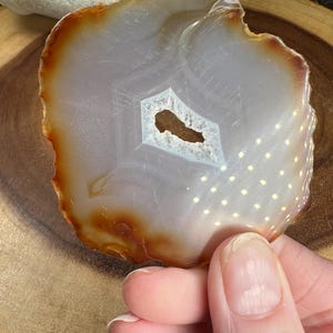 May include: A white agate slice with a brown edge and a small hole in the centre. The agate has a white and brown pattern.