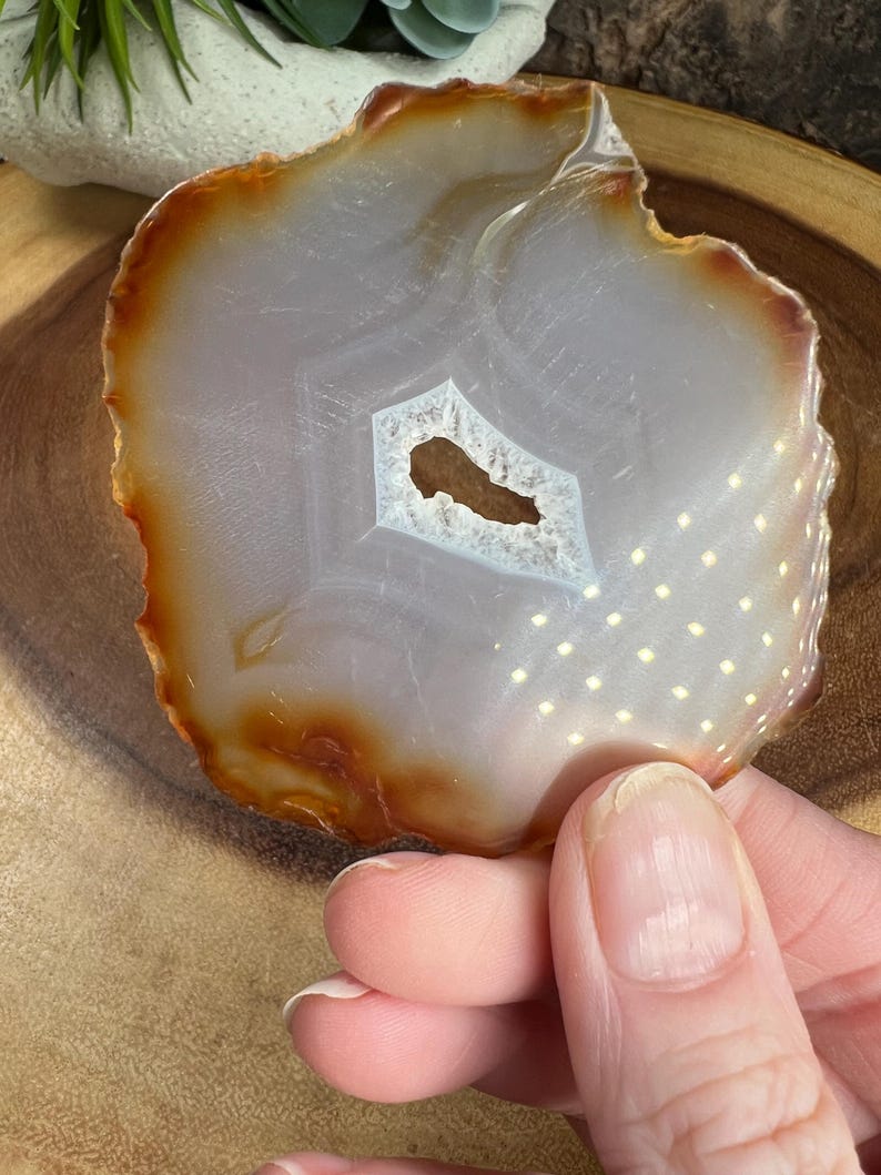 May include: A white agate slice with a brown edge and a small hole in the centre. The agate has a white and brown pattern.