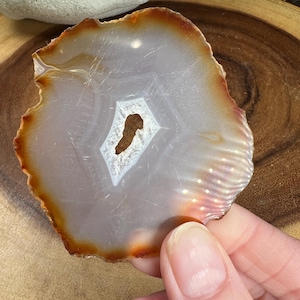 May include: A white agate slice with a brown edge. The agate has a natural hole in the center.