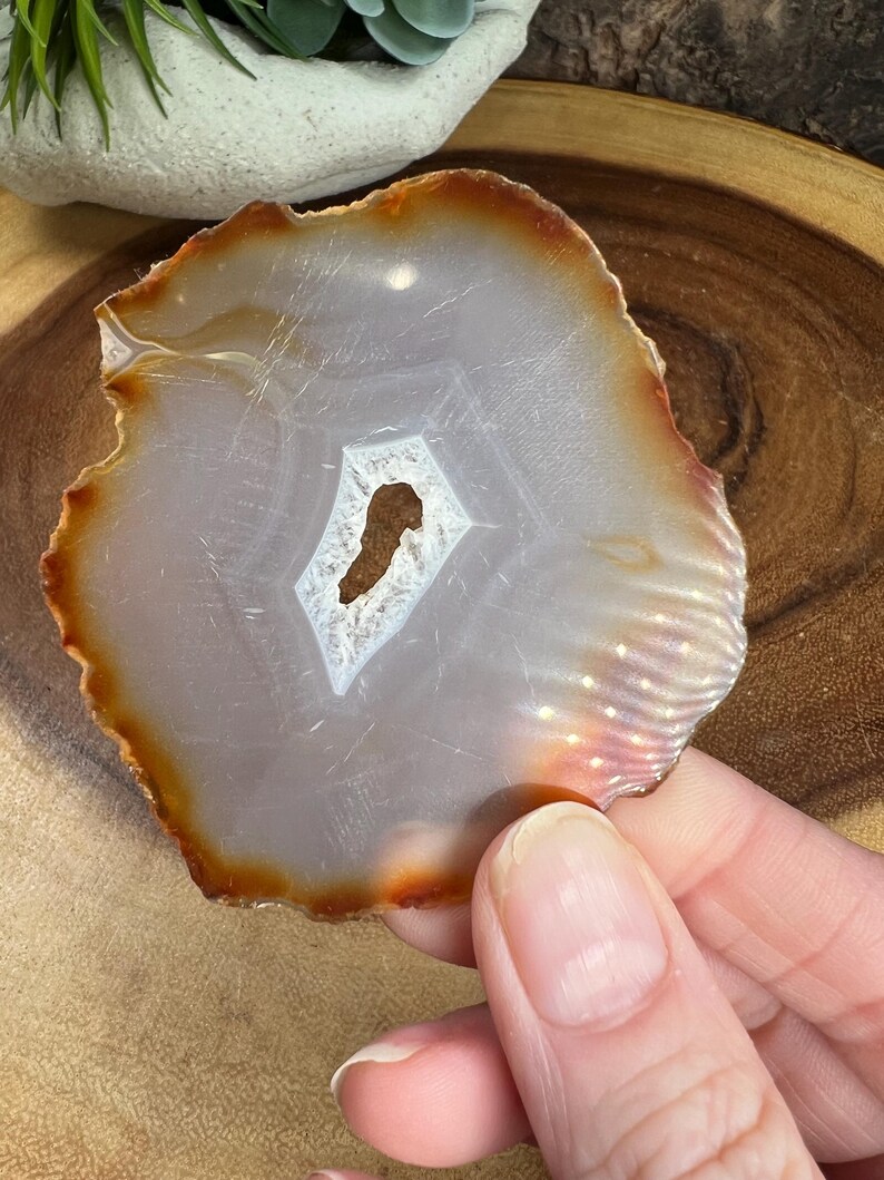 May include: A white agate slice with a brown edge. The agate has a natural hole in the centre.