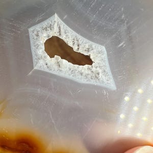 May include: Close-up of a light grey agate slice with a large, irregular hole in the centre. The agate has a brown band around the edge.