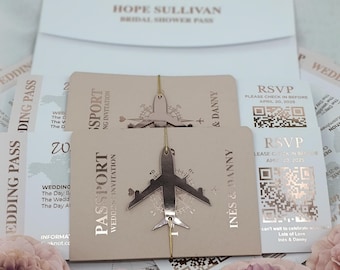May include: A set of wedding invitations with a passport and airplane theme. The invitations are pink and gold with a gold airplane charm. The text on the invitations reads "Passport Wedding Invitation" and "RSVP Please check in before April 20, 2025".