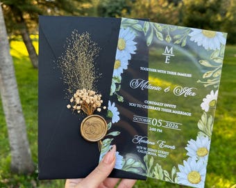 Könnte beinhalten: Transparente Acryl-Hochzeitseinladung mit weißen Gänseblümchen und grünen Blättern. Die Einladung zeigt den Text "Melanie & Alex" und "Oktober 05, 2026" in schwarzer Schreibschrift. Die Einladung enthält auch den Text "Gardena Events" und Kontaktinformationen.