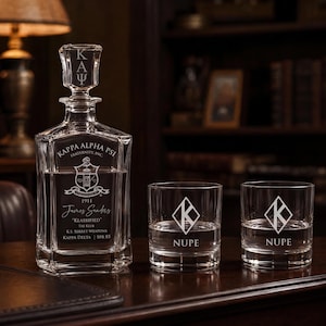 May include: A clear glass decanter with a stopper and two matching whiskey glasses. The decanter features the Kappa Alpha Psi crest, the name James Sanders, and the text Klassified. The glasses are etched with a diamond K logo and the word NUPE.