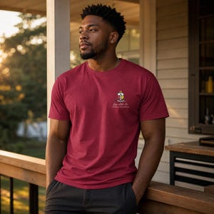 May include: A maroon short-sleeved crew neck t-shirt featuring a small, colorful Kappa Alpha Psi fraternity crest and the text "Kappa Alpha Psi" printed on the left chest area. The shirt is made of a solid-colored fabric with a standard fit.