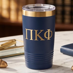 May include: A navy blue insulated tumbler with a clear lid and a metallic gold rim. The front of the tumbler features the Greek letters Pi Kappa Phi in a bold, gold-colored font. The base of the tumbler has a series of horizontal ridges.
