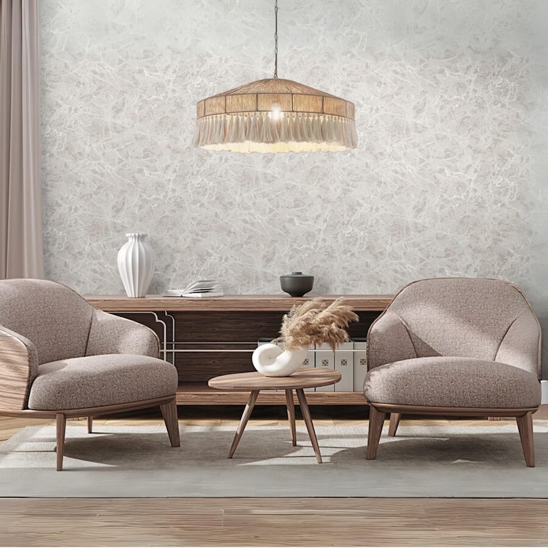 May include: A living room scene featuring two beige armchairs, a wooden coffee table, and a wooden cabinet. A large, round pendant light with a woven shade and fringe hangs from the ceiling. The walls have a textured, light gray pattern.