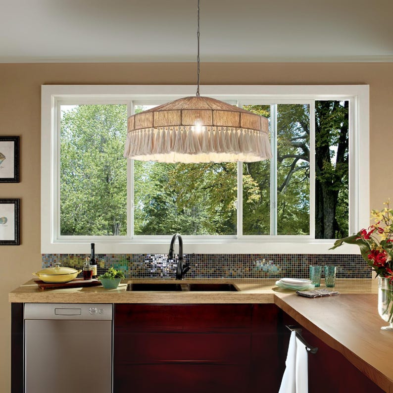 May include: A kitchen with a large window overlooking trees. A woven pendant light with fringe hangs above the sink. The kitchen has a dark wood countertop and cabinets, with a stainless steel dishwasher.