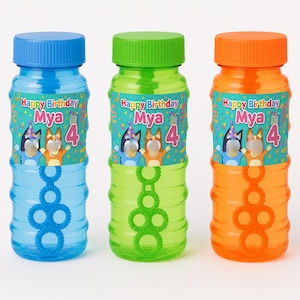 May include: Three plastic bubble solution bottles in blue, green, and orange. Each bottle features a label with the text Happy Birthday Mya 4, decorated with colorful confetti and illustrations of two cartoon dogs wearing party hats.