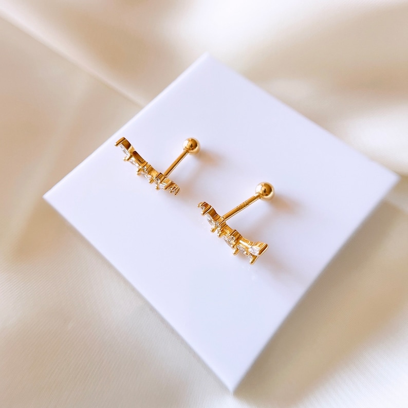 Op de afbeelding: Een paar gouden oormanchetten met een gebogen ontwerp en heldere zirkonia-stenen.